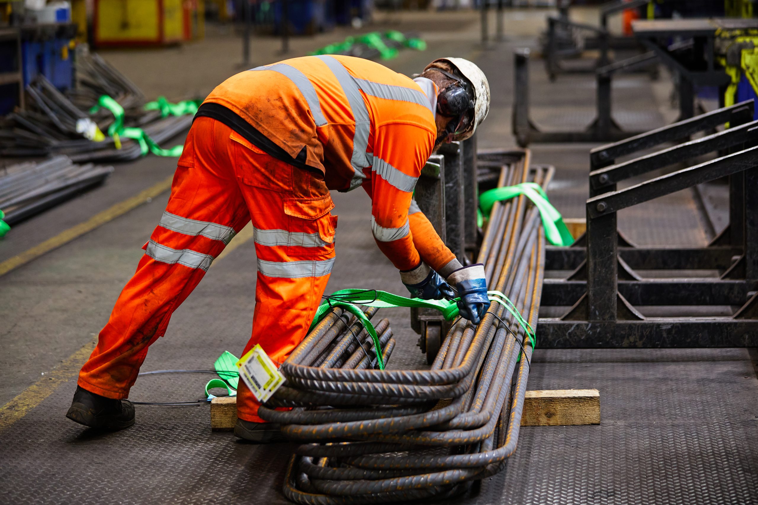 A steel mill worker wearing safety gear, operating machinery working with molten metal and industrial equipment.
